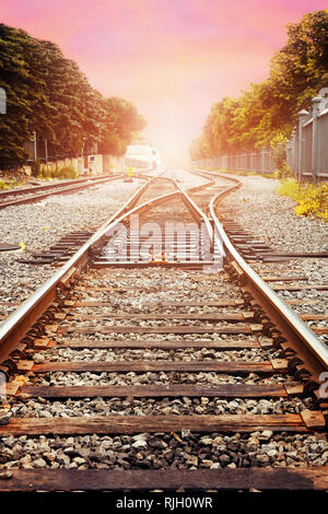 I binari della ferrovia contro il bellissimo cielo al tramonto. Paesaggio industriale con la ferrovia, pastello colorato cielo di nuvole, sole e alberi. Foto Stock