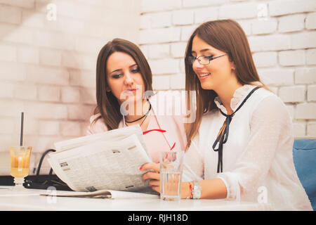 Sorridente due giovani donne della pianificazione della loro strategia di business pur avendo pausa caffè e discutere di notizie. Foto Stock