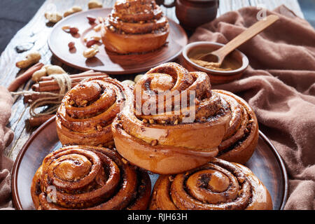 Pane appena sfornato panini alla cannella panini con arachidi servita su un piatto di terracotta e due tazze di caffè in background. Svedese Kanelbulle dessert, vie Foto Stock