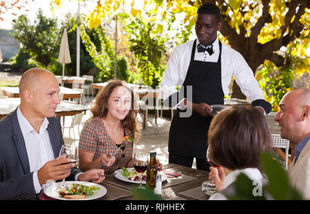 Cameriere che serve pasti al cordiale compagnia presso il ristorante all'aperto Foto Stock