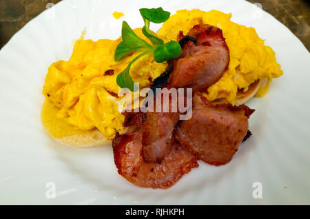 La prima colazione snack nello Yorkshire tostati muffin inglese con due fettine di pancetta e uova strapazzate Foto Stock