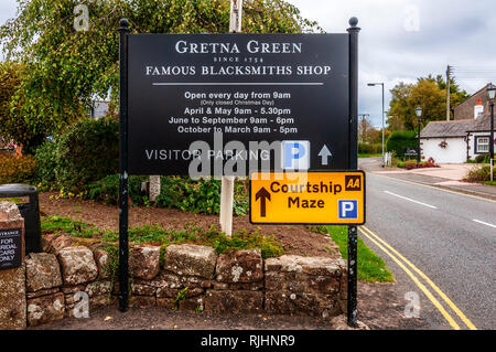 Un grande nero bacheca all'entrata a Gretna Green famoso fabbri shop, con caratteri bianchi pubblicità e dando tempi di apertura Foto Stock