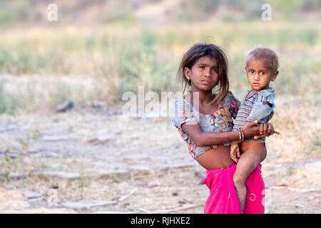 Una giovane ragazza dalla tribù Bhil detiene un giovane maschio in Rajasthan rurale vicino Bhainsrorgargh, India. Foto Stock