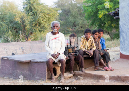 Tribù Bhil. Un uomo anziano si siede con quattro giovani ragazzi nel loro villaggio vicino Bhainsrorgargh, Rajasthan, India. Foto Stock