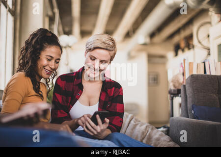 Giovani amici adulti socializzare mentre sui loro smartphone Foto Stock