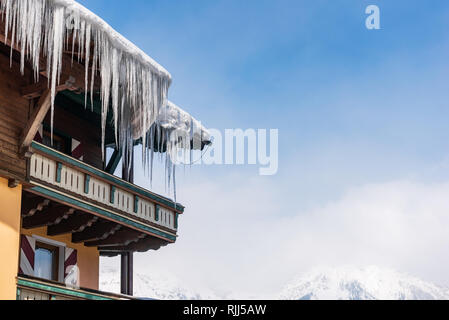 Grandi ghiaccioli appesi sopra la grondaia pioggia su un tetto di una tradizionale casa in legno in montagna in inverno potrebbe essere pericoloso. Foto Stock
