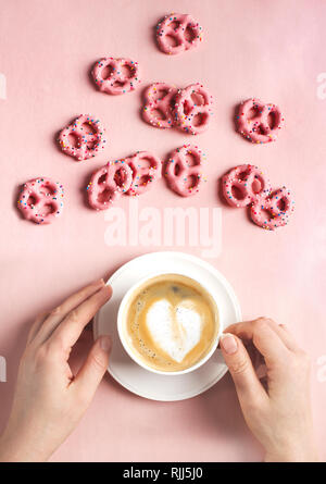 Mani femminili tenere tazza di caffè con arte forma di cuore su sfondo rosa. Il concetto di amore. Piatto, laici vista superiore Foto Stock