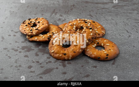 Vista laterale di un piccolo mucchio di morso dimensioni bagel chip con semi assortiti su sfondo grigio illuminato con luce naturale. Foto Stock