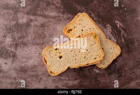 Vista dall'alto di due fette di segale Melba toast su uno sfondo marrone rossiccio illuminato con luce naturale. Foto Stock