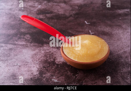 Vista laterale di una piccola ciotola riempita con zucchero libero di salsa di mele con un cucchiaio nel cibo su un sfondo marrone rossiccio. Foto Stock