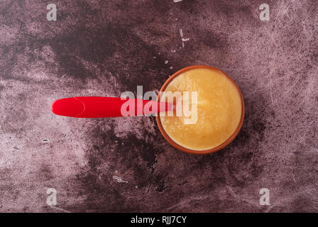 Vista aerea di una piccola ciotola riempita con zucchero libero di salsa di mele con un cucchiaio nel cibo su un sfondo marrone rossiccio. Foto Stock