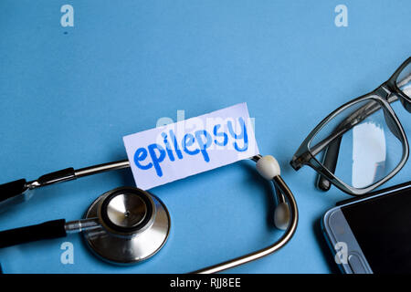 Immagine concettuale con epilessia iscrizione con la vista di uno stetoscopio, occhiali e smartphone su sfondo blu. Medical concettuale. Foto Stock