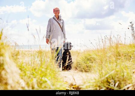 Donna cammina con il suo cane, re poodle, in dune sul mare, Portbail, Normandia, Francia Foto Stock