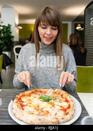 Ritratto di giovane donna di mangiare la pizza. Pizza Napoletana da stufa a legna. Pranzo in una trattoria italiana. Tabella vicino ad una grande finestra. Margarita Foto Stock