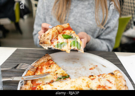 Una donna è mangiare pizza napoletana dalla stufa a legna. Il pranzo in un ristorante italiano. Tabella vicino ad una grande finestra. Margarita e quattro formaggi Foto Stock