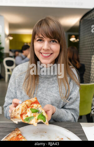 Una donna è mangiare pizza napoletana dalla stufa a legna. Il pranzo in un ristorante italiano. Tabella vicino ad una grande finestra. Margarita e quattro formaggi Foto Stock