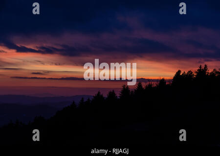 Alberi sagome contro un colore bellissimo cielo al tramonto, con montagne di strati in background Foto Stock