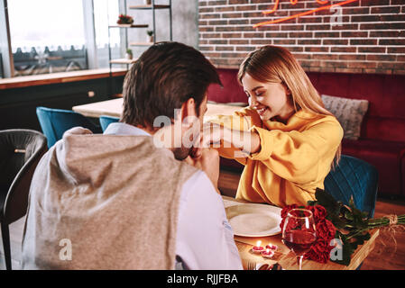 Proposta romantica. Giovane uomo bacia le mani della sua fidanzata nel ristorante. Rose rosse e candele sono giacenti sul tavolo vicino al vino rosso. Pho ritagliata Foto Stock