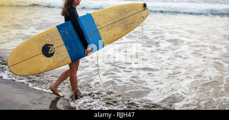 Giovane e attraente felice surfer girl nella bellissima spiaggia che trasportano il giallo della tavola da surf passeggiate nell'oceano godendo le vacanze estive a Isola tropicale