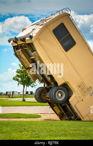 An unsettling view of an old RV buried nose first into the ground with back half of the RV lifted up towards the sky at a roadside attraction in TX Foto Stock