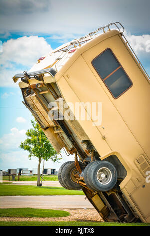 An unsettling view of an old RV buried nose first into the ground with back half of the RV lifted up towards the sky at a roadside attraction in TX Foto Stock