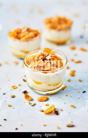 Sana colazione o dessert. Gustosi corn flakes con yogurt, mandorla e miele in un bicchiere piccolo su fondo azzurro. Copia spazio per il testo. Foto Stock