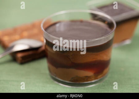Ciotola con deliziosa crema di cioccolato, cucchiaio e i dadi sul tavolo di legno Foto Stock
