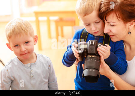 Infanzia felice. La madre ed i suoi figli ragazzi bambini che giocano con la fotocamera di scattare una foto a casa. Foto reale Foto Stock