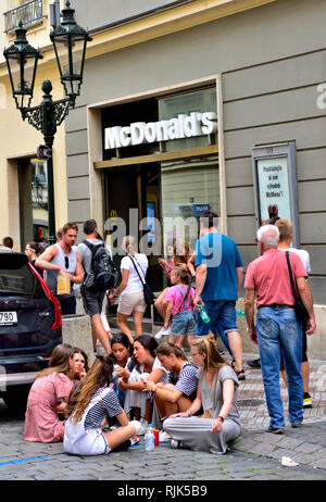 Gente seduta sul marciapiede e la strada al di fuori di McDonald in Prague di mangiare fast food Foto Stock