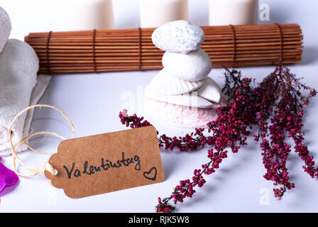 Una etichetta dicendo "Valentinstag' e colorato in rosso i rami, pietre, candele e un tappetino di bambù su sfondo bianco con spazio di copia Foto Stock