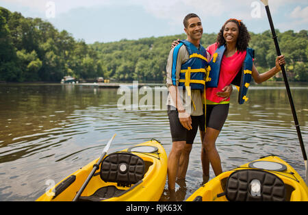 Ritratto di un sorridente coppia giovane abbracciando nella parte anteriore del loro kayak. Foto Stock