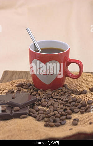 Tazza di caffè con caffè torrefatto in grani accanto ad alcuni di cioccolato nero compresse, su un vecchio tavolo in legno Foto Stock