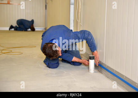 Tradesman maschere off l'altezza delle arcate prima di applicare il prodotto epossidico al piano di un edificio industriale Foto Stock