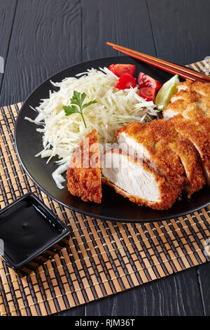 Tonkatsu - panko panate fritte cotoletta di maiale servito con fresco grattugiato insalata di cavolo, pomodori e fettine di lime su una piastra, la cucina giapponese, verti Foto Stock