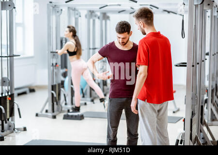 Terapista di parlare con l'uomo paziente avendo problemi con il suo ritorno in piedi presso la palestra di riabilitazione Foto Stock