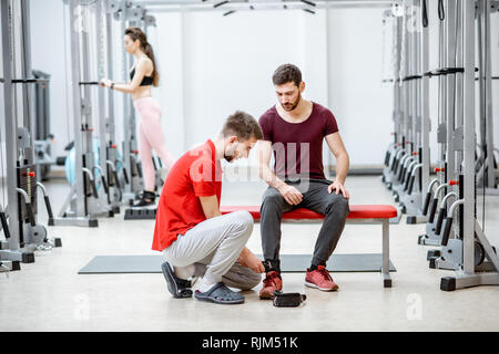 Trainer indossare polsini sulle gambe del paziente la preparazione per gli esercizi in palestra di riabilitazione Foto Stock