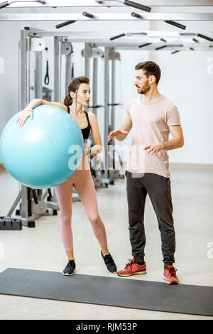 Allenatore sportivo con la giovane donna tenendo palla fitness, insieme permanente presso la palestra di riabilitazione Foto Stock