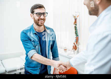 L'uomo come un handshaking di paziente con senior medico visita terapista office Foto Stock