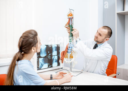 Giovane donna durante la consultazione medica con i senior terapista che mostra il modello della colonna vertebrale in ufficio Foto Stock