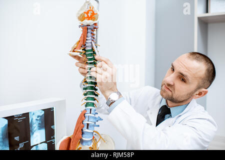 Senior terapista che mostra il modello anatomico della colonna vertebrale umana durante la consultazione in ufficio Foto Stock