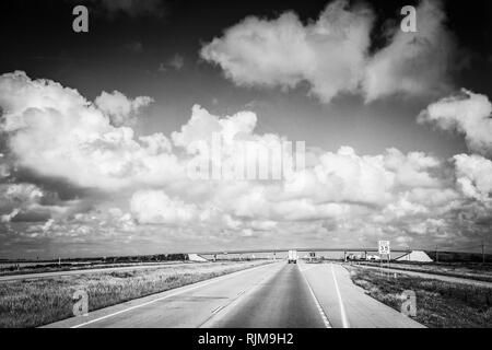 La guida verso il basso che lungo, Lonesome Highway con infinite big sky e nuvole nel piatto paesaggio del Texas Foto Stock