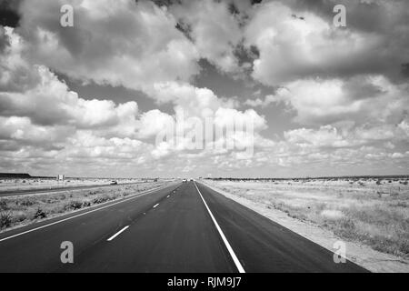 La guida verso il basso che lungo, Lonesome Highway con infinite big sky e nuvole nel piatto paesaggio del Texas in bianco e nero Foto Stock