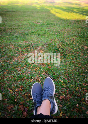 Donna di gambe in scarpe grigio a sedersi su foglie secche nel parco. Foto Stock