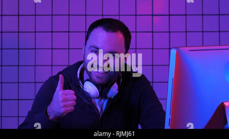 Gioiosa gamer guy riproduzione di video giochi sul computer e che mostra il pollice fino alla telecamera. Foto Stock