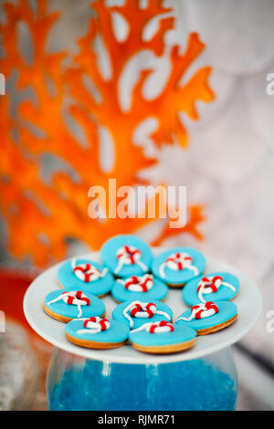 Grande piastra bianca con un sacco di pane di zenzero i biscotti con blu brillante di glassa e tempo di mare d cor. Arancione coralli in legno sullo sfondo. Foto Stock