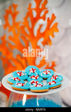 Grande piastra bianca con un sacco di pane di zenzero i biscotti con blu brillante di glassa e tempo di mare d cor. Arancione coralli in legno sullo sfondo. Foto Stock