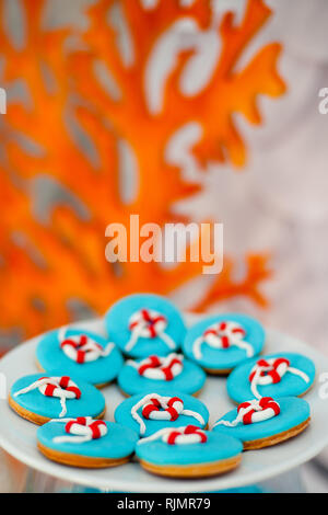 Grande piastra bianca con un sacco di pane di zenzero i biscotti con blu brillante di glassa e tempo di mare d cor. Arancione coralli in legno sullo sfondo. Foto Stock