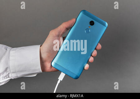 Mano d'uomo tenendo lo smartphone con il cavo usb Foto Stock