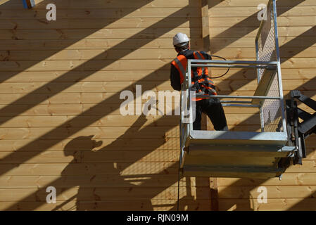 Tradesman verniciatura a spruzzo la parete del legno di un edificio industriale con il preservante del legno Foto Stock