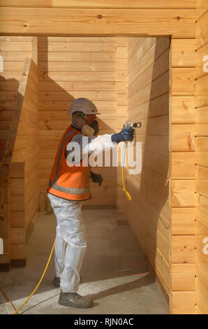 Tradesman verniciatura a spruzzo la parete del legno di un edificio industriale con il preservante del legno Foto Stock